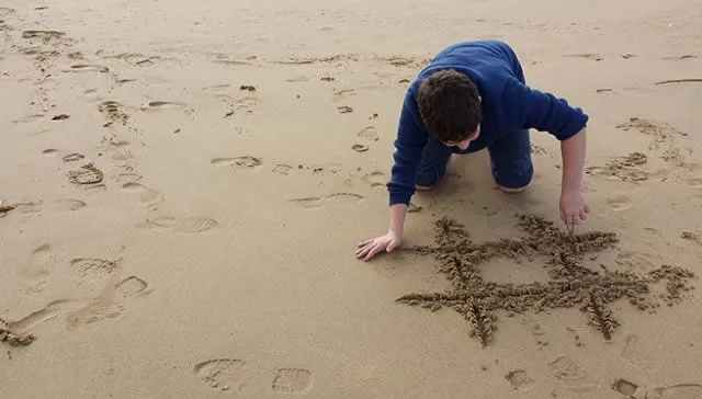 Мальчик пишет хештег на морском песке